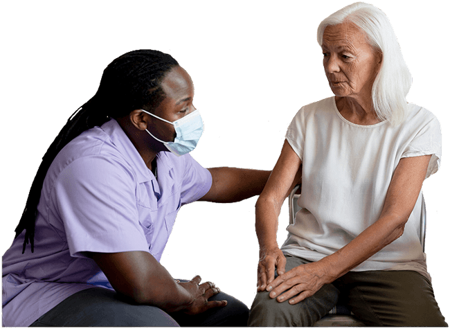 A caregiver with a hand on the shoulder of an older woman, listening to her.